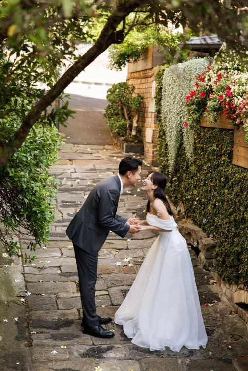 Frank and Seoyun holding hands on a flower-strewn laneway staircase