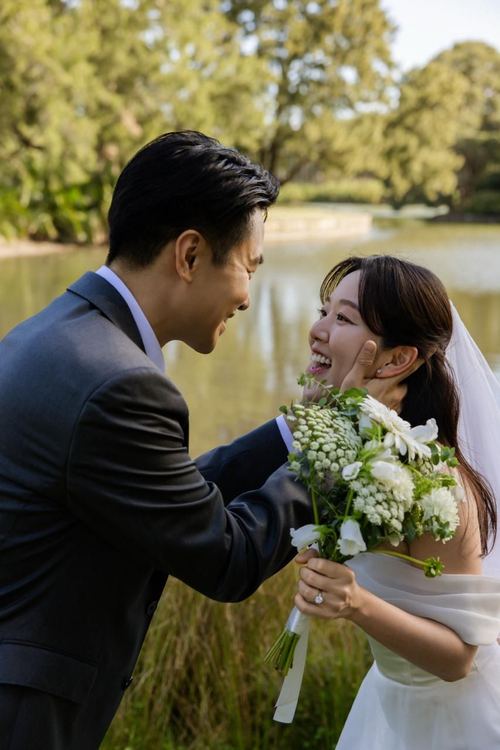 Frank cupping Seoyun's face beside the garden lake, bouquet in hand